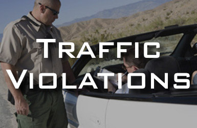 A police officer stands beside a car, speaking to the driver on a desert road. The words "Traffic Violations" are prominently overlaid on the image.