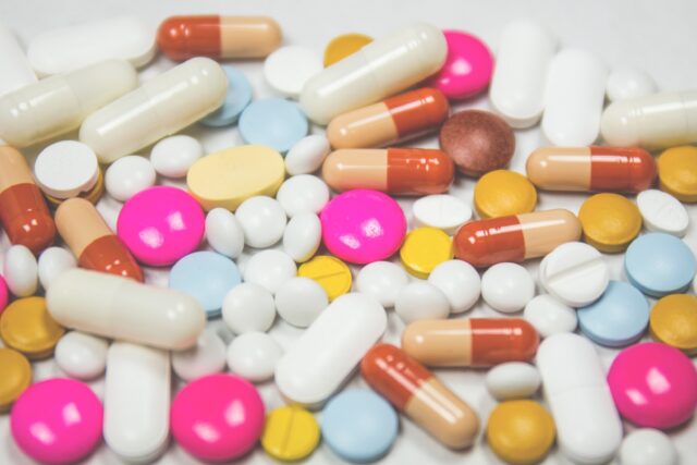 A variety of colorful pills and capsules, reminiscent of a New York pharmacy scene, are scattered on a white surface. Pink, yellow, blue, and orange tablets mingle with white, orange, and beige capsules—highlighting the vivid spectrum often associated with drug crimes and their consequences. Garden City Prescription Drug Charges Lawyer concept image