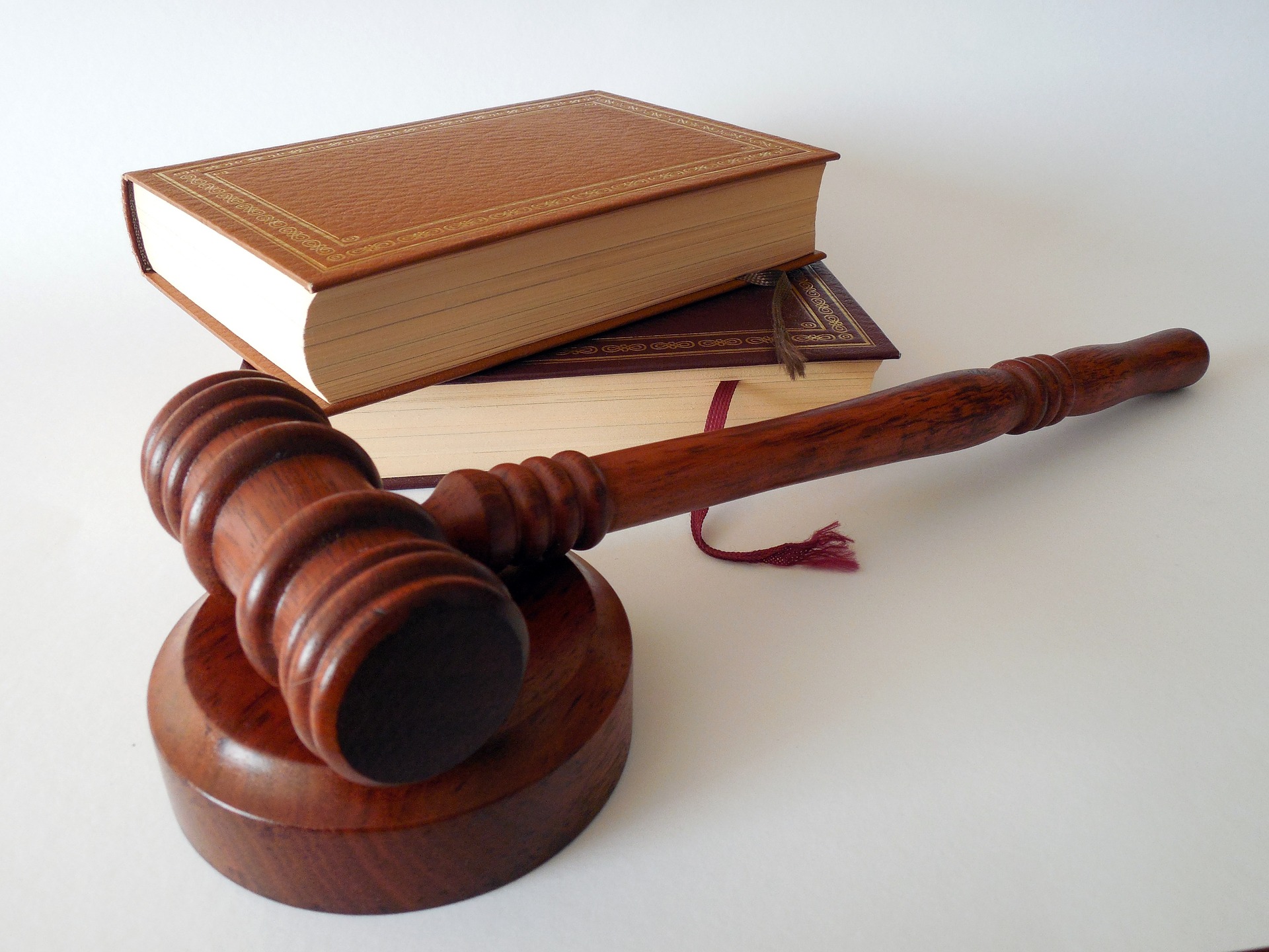 A wooden gavel rests on a round base in the foreground. Behind it, two thick, closed law books with textured brown covers are stacked on a white surface, symbolizing justice for cases involving drunk drivers.