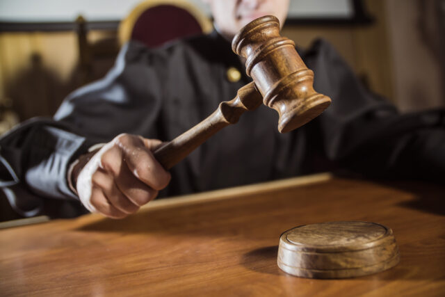 A judge's hand strikes a wooden gavel onto a sound block on the table, emphasizing the gravity of the case. Clad in a black robe, the judge presides over matters that often require the expertise of a cocaine possession lawyer in this solemn courtroom setting.