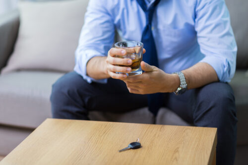 Man holding drink with car keys on table