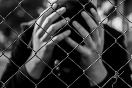 juvenile with hands on head behind a fence