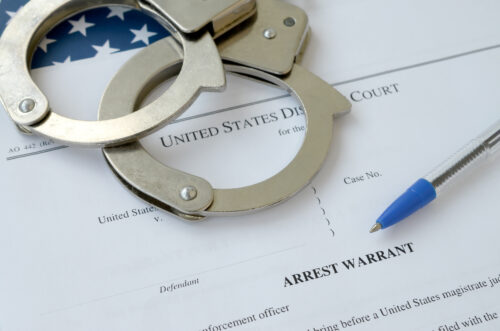 District Court Arrest Warrant court papers with handcuffs and blue pen on United States flag