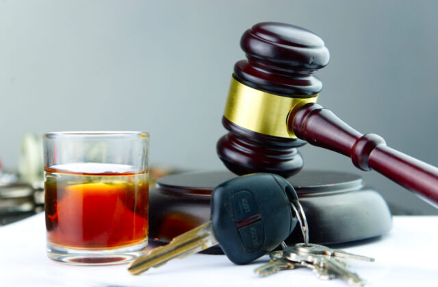 A judge's gavel, a glass of alcohol, and car keys are placed together on a table, symbolizing the legal consequences of drinking and driving.
